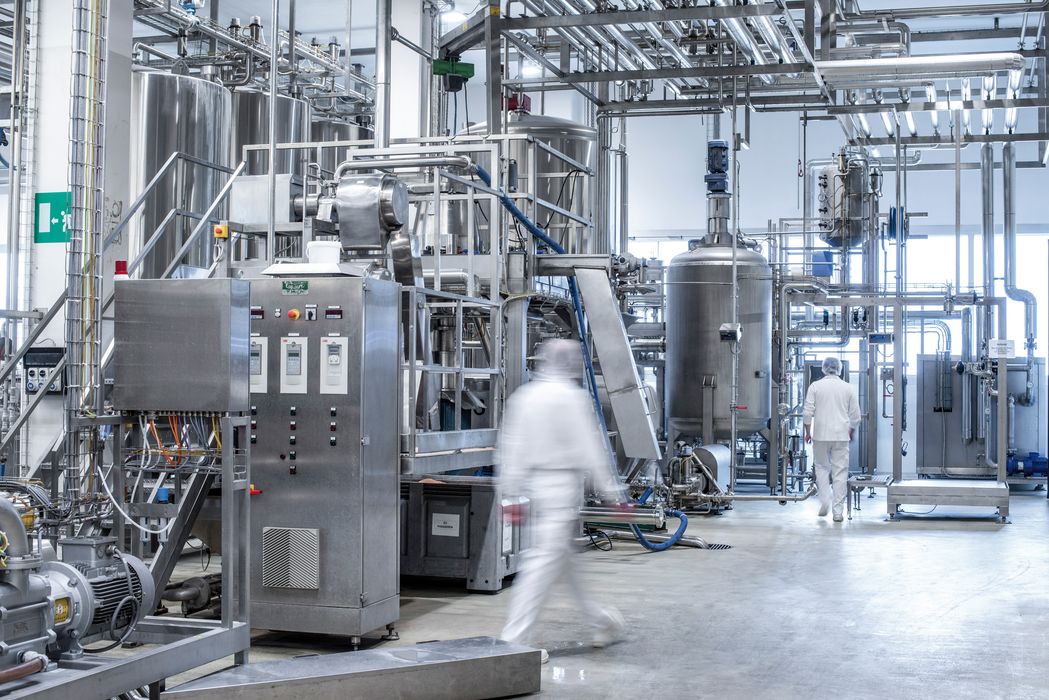 Moderne Lebensmittel- oder Pharmaindustrie mit Edelstahlbehältern, Rohrleitungen und zwei Personen in weißer Arbeitskleidung