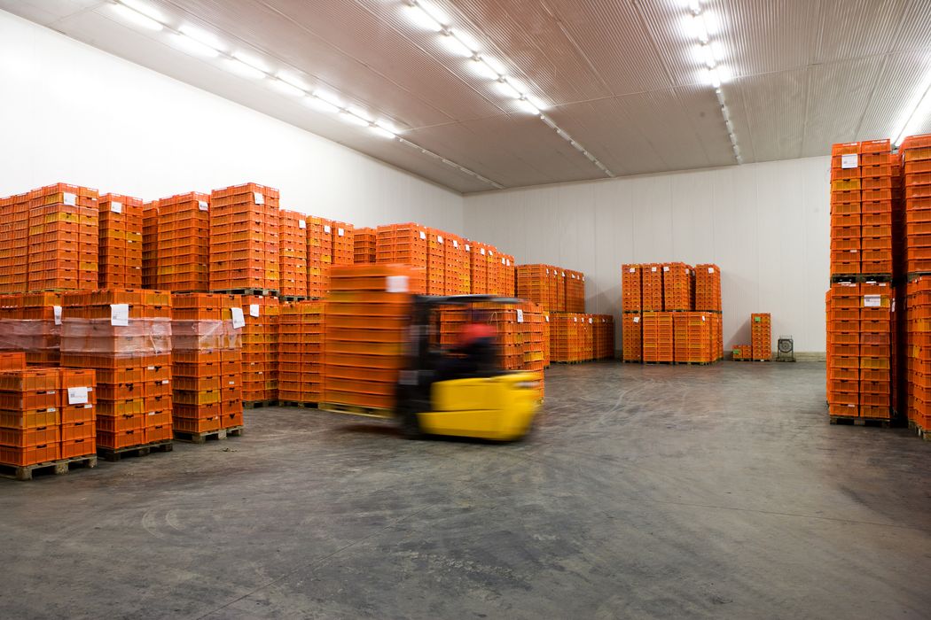Lagerhalle mit vielen gestapelten orangen Kisten und einem gelben Gabelstapler in Bewegung
